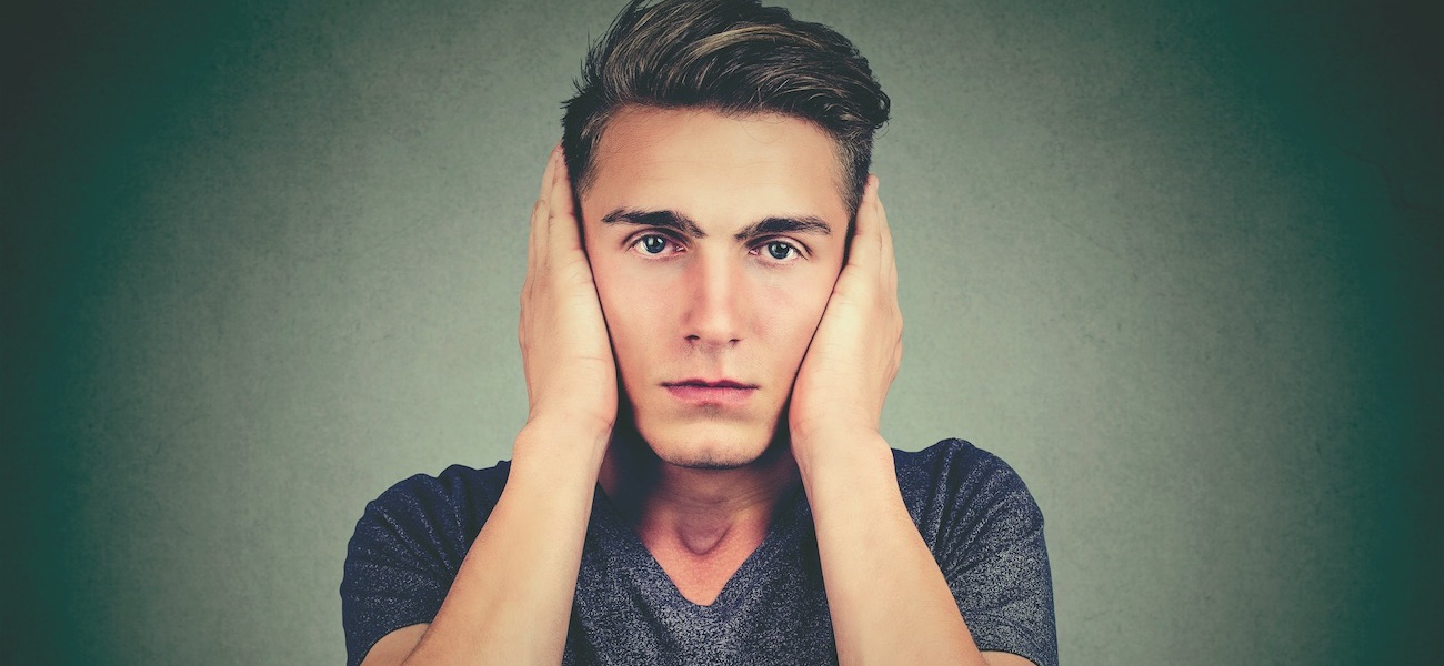 Portrait of a tranquil relaxed man covering his ears looking at camera isolated on gray background. Hear no evil concept. Human emotions